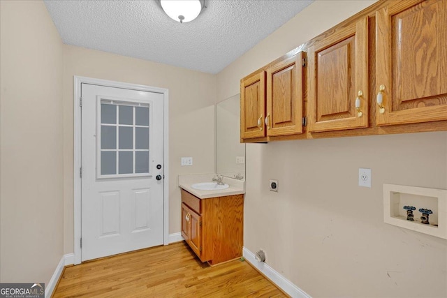 laundry room featuring cabinets, electric dryer hookup, hookup for a washing machine, a textured ceiling, and light wood-type flooring