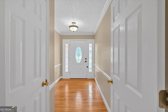 entryway with light wood-type flooring, a textured ceiling, and ornamental molding