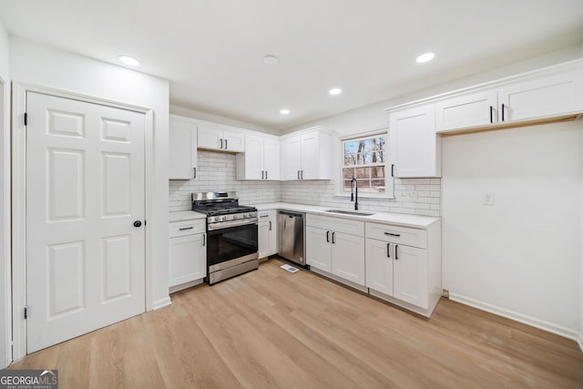 kitchen with white cabinets, sink, light wood-type flooring, appliances with stainless steel finishes, and tasteful backsplash