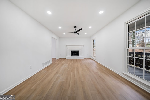 unfurnished living room with ceiling fan, a fireplace, and light wood-type flooring