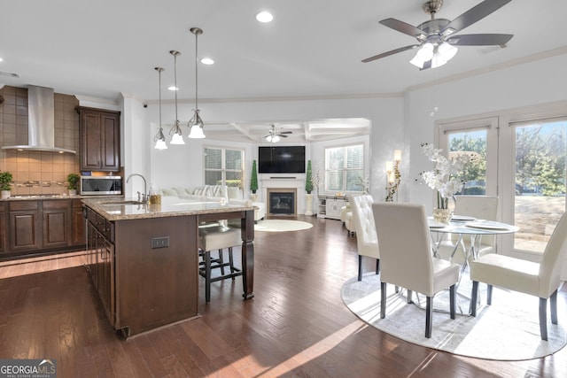 kitchen featuring a breakfast bar, a kitchen island with sink, wall chimney range hood, sink, and tasteful backsplash