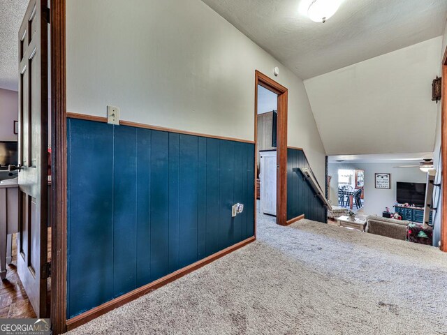 interior space featuring dark carpet, a textured ceiling, wooden walls, and vaulted ceiling