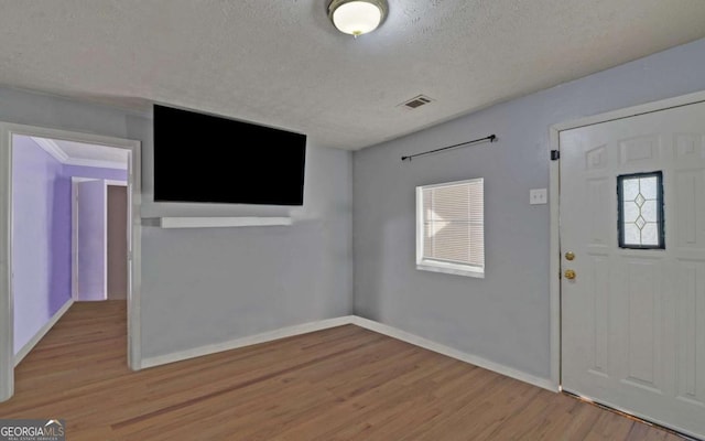 entryway with ornamental molding, a textured ceiling, and light hardwood / wood-style flooring