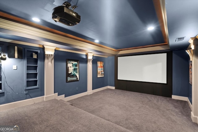 carpeted home theater featuring decorative columns, a tray ceiling, and ornamental molding