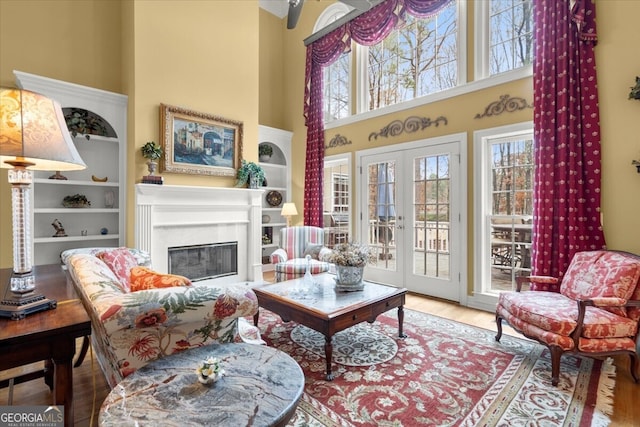 living room featuring built in shelves, french doors, a high ceiling, a fireplace, and hardwood / wood-style flooring