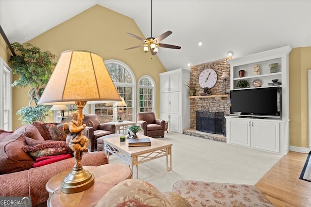 living room with high vaulted ceiling, light hardwood / wood-style floors, a stone fireplace, and ceiling fan