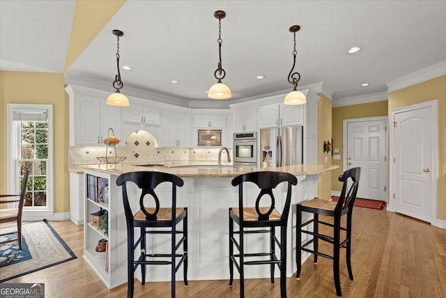 kitchen with stainless steel appliances, light stone counters, light hardwood / wood-style floors, a center island with sink, and white cabinets