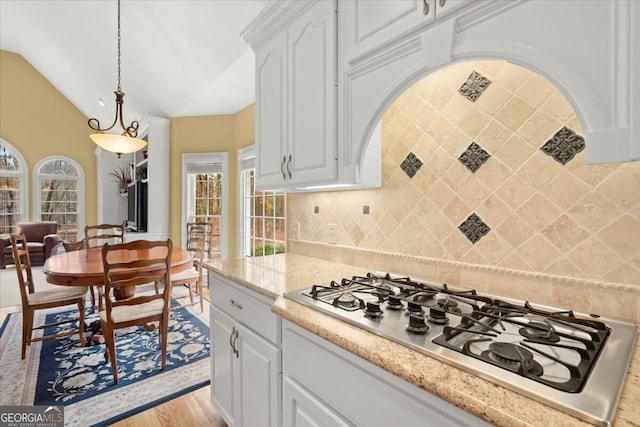 kitchen with stainless steel gas stovetop, white cabinets, light hardwood / wood-style flooring, decorative backsplash, and decorative light fixtures