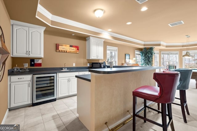 kitchen featuring white cabinetry, sink, wine cooler, pendant lighting, and a breakfast bar area