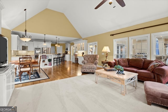 living room featuring ceiling fan, light hardwood / wood-style flooring, and high vaulted ceiling