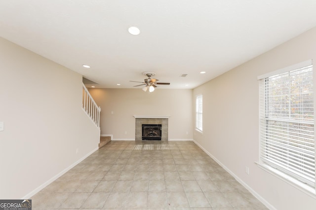 unfurnished living room featuring light tile patterned flooring, ceiling fan, plenty of natural light, and a tiled fireplace