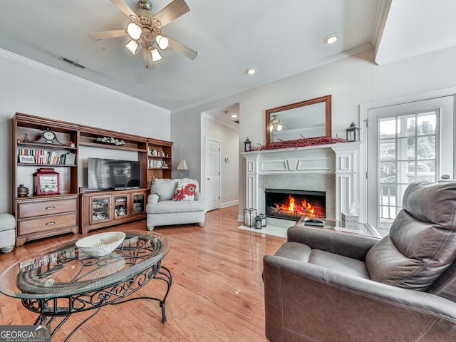 living room featuring crown molding, a fireplace, ceiling fan, and light wood-type flooring