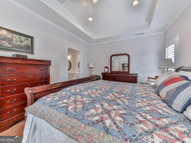 bedroom with ensuite bath, ornamental molding, a tray ceiling, ceiling fan, and light hardwood / wood-style flooring