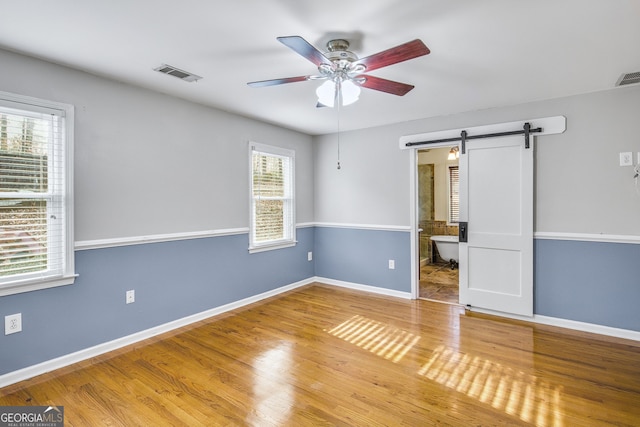 unfurnished bedroom with multiple windows, a barn door, ensuite bath, and ceiling fan