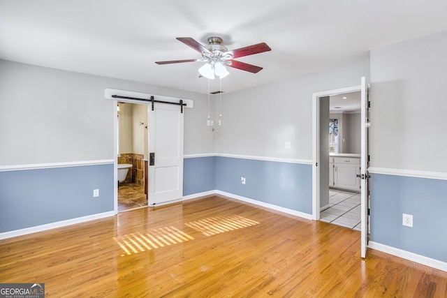 spare room featuring a barn door, ceiling fan, and light wood-type flooring