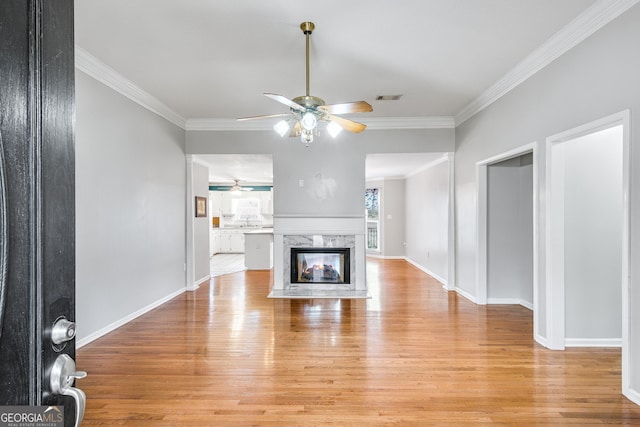 unfurnished living room featuring ceiling fan, a high end fireplace, ornamental molding, and light wood-type flooring