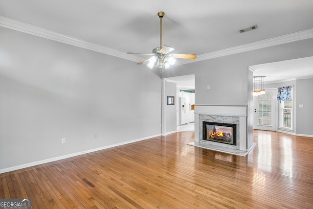 unfurnished living room with ceiling fan, crown molding, a high end fireplace, and light wood-type flooring