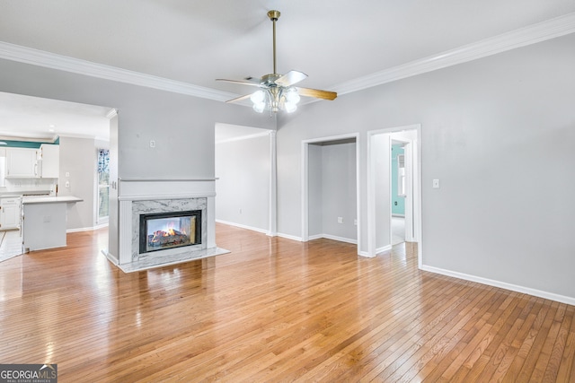 unfurnished living room featuring a high end fireplace, light wood-type flooring, ceiling fan, and ornamental molding