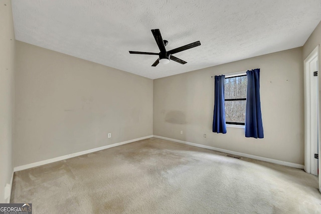 empty room with ceiling fan, light colored carpet, and a textured ceiling