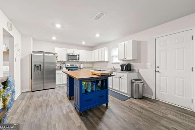 kitchen with wood counters, white cabinetry, blue cabinets, and appliances with stainless steel finishes