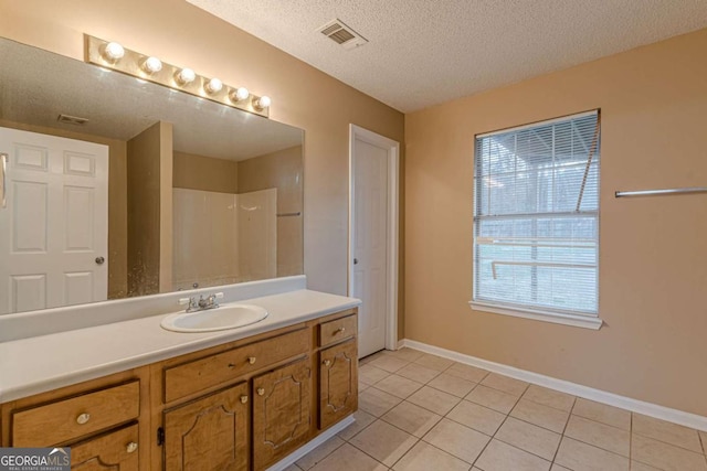 bathroom featuring tile patterned flooring, vanity, a textured ceiling, and walk in shower