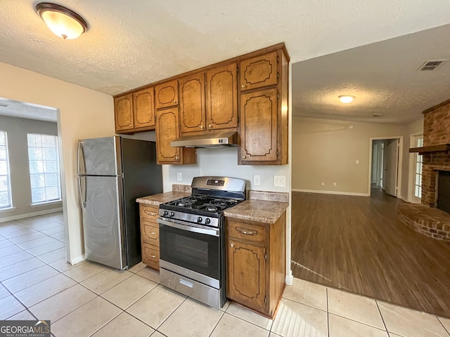 kitchen featuring a brick fireplace, a textured ceiling, appliances with stainless steel finishes, and light hardwood / wood-style flooring