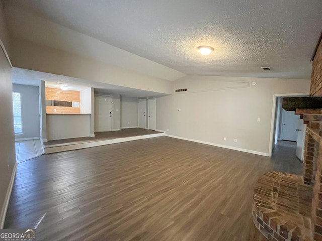 unfurnished living room featuring a textured ceiling, a fireplace, dark hardwood / wood-style flooring, and vaulted ceiling