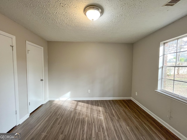 spare room with a textured ceiling and dark wood-type flooring