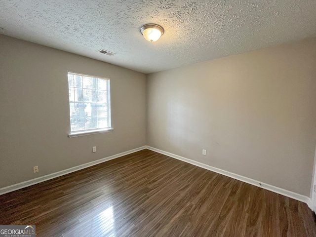 spare room featuring a textured ceiling and dark hardwood / wood-style floors