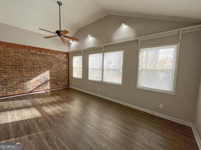 spare room with dark hardwood / wood-style floors, brick wall, a wealth of natural light, and vaulted ceiling