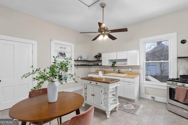 kitchen with ceiling fan, white cabinetry, sink, and gas range