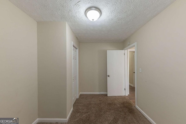 hall with dark carpet and a textured ceiling