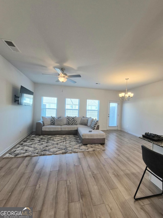 living room with ceiling fan with notable chandelier and light hardwood / wood-style floors