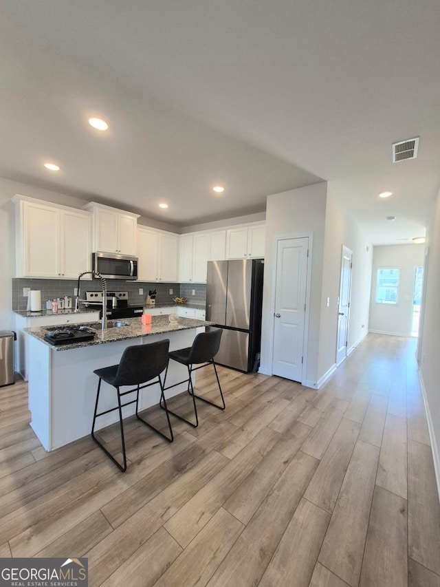 kitchen featuring white cabinetry, stainless steel appliances, backsplash, dark stone countertops, and light hardwood / wood-style floors