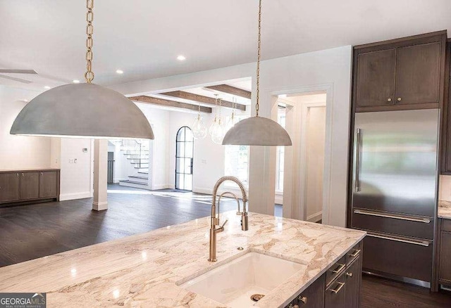 kitchen featuring sink, built in refrigerator, dark hardwood / wood-style floors, beamed ceiling, and light stone counters