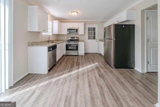 kitchen with light stone countertops, white cabinetry, sink, stainless steel appliances, and light wood-type flooring