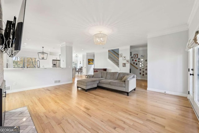 living room with a chandelier, sink, crown molding, and light hardwood / wood-style flooring