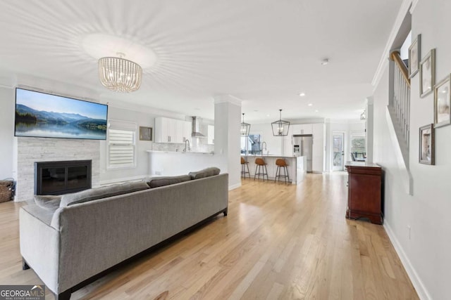 living room featuring a fireplace, light hardwood / wood-style floors, an inviting chandelier, and crown molding