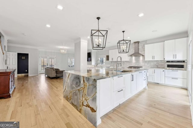 kitchen featuring oven, wall chimney exhaust hood, light wood-type flooring, decorative light fixtures, and white cabinetry