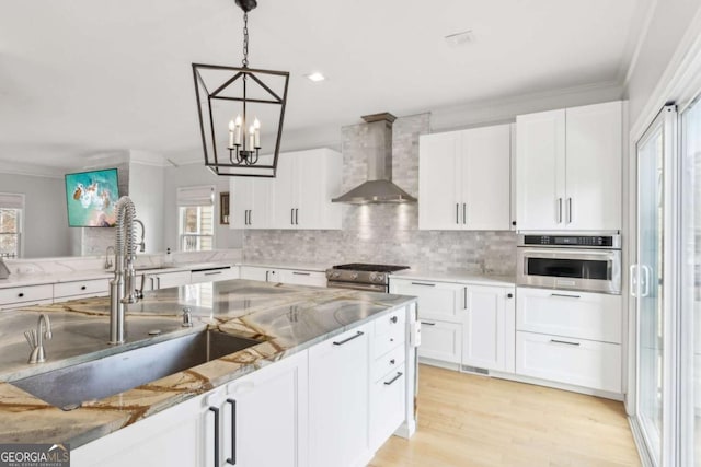 kitchen featuring stainless steel appliances, sink, wall chimney range hood, white cabinets, and hanging light fixtures