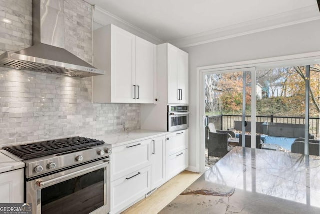 kitchen with backsplash, light stone counters, wall chimney exhaust hood, stainless steel appliances, and white cabinets