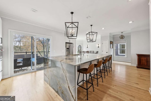 kitchen with light wood-type flooring, light stone counters, high end fridge, a spacious island, and decorative light fixtures