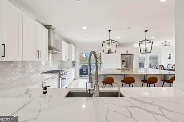 kitchen featuring wall chimney exhaust hood, sink, decorative light fixtures, white cabinetry, and a breakfast bar area