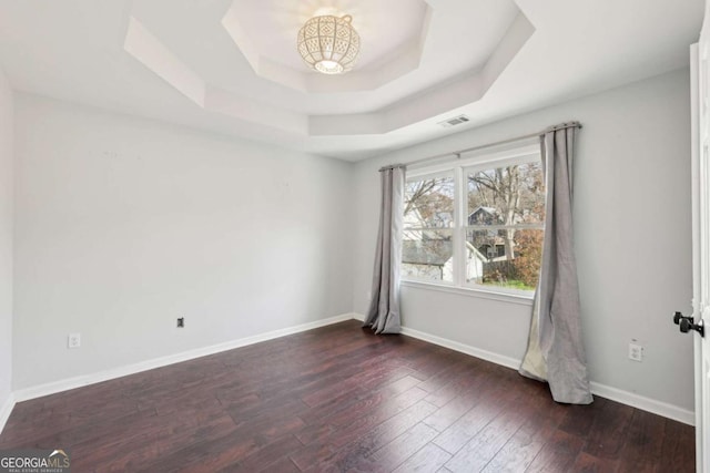 unfurnished room featuring a tray ceiling and dark wood-type flooring