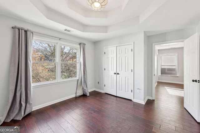 unfurnished bedroom with a tray ceiling, a closet, and dark hardwood / wood-style floors