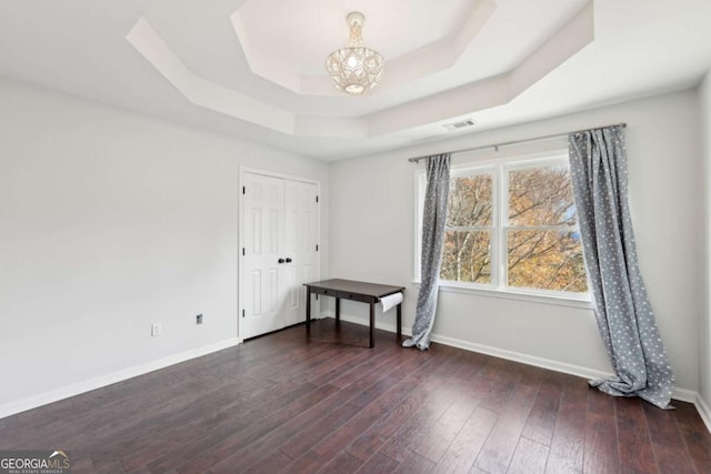 unfurnished bedroom featuring a raised ceiling, dark hardwood / wood-style flooring, and a chandelier