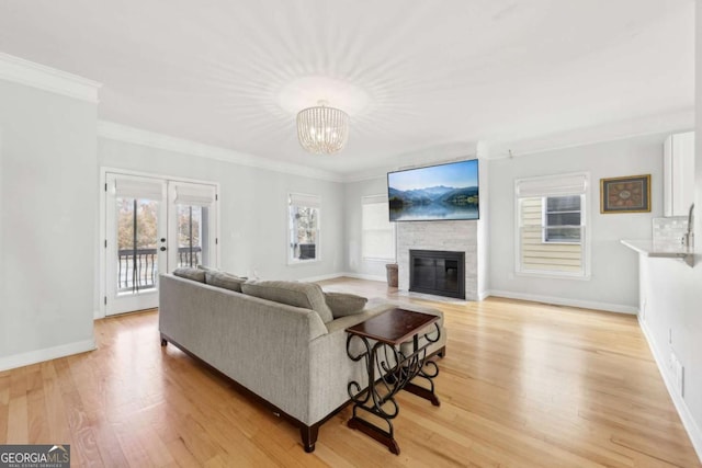 living room featuring french doors, light wood-type flooring, ornamental molding, a large fireplace, and a notable chandelier