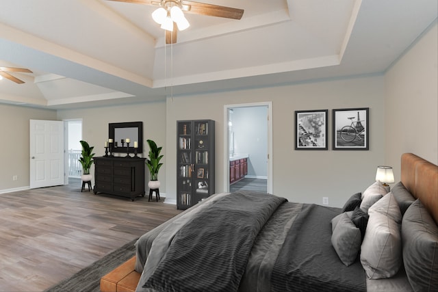 bedroom with hardwood / wood-style floors, connected bathroom, a raised ceiling, and ceiling fan