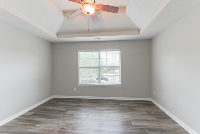 unfurnished room featuring a textured ceiling, dark hardwood / wood-style floors, ceiling fan, and a tray ceiling