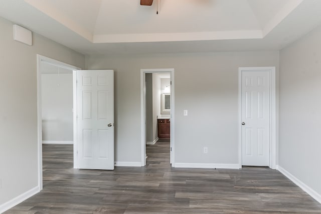 unfurnished bedroom featuring dark hardwood / wood-style floors, a raised ceiling, ceiling fan, and ensuite bathroom